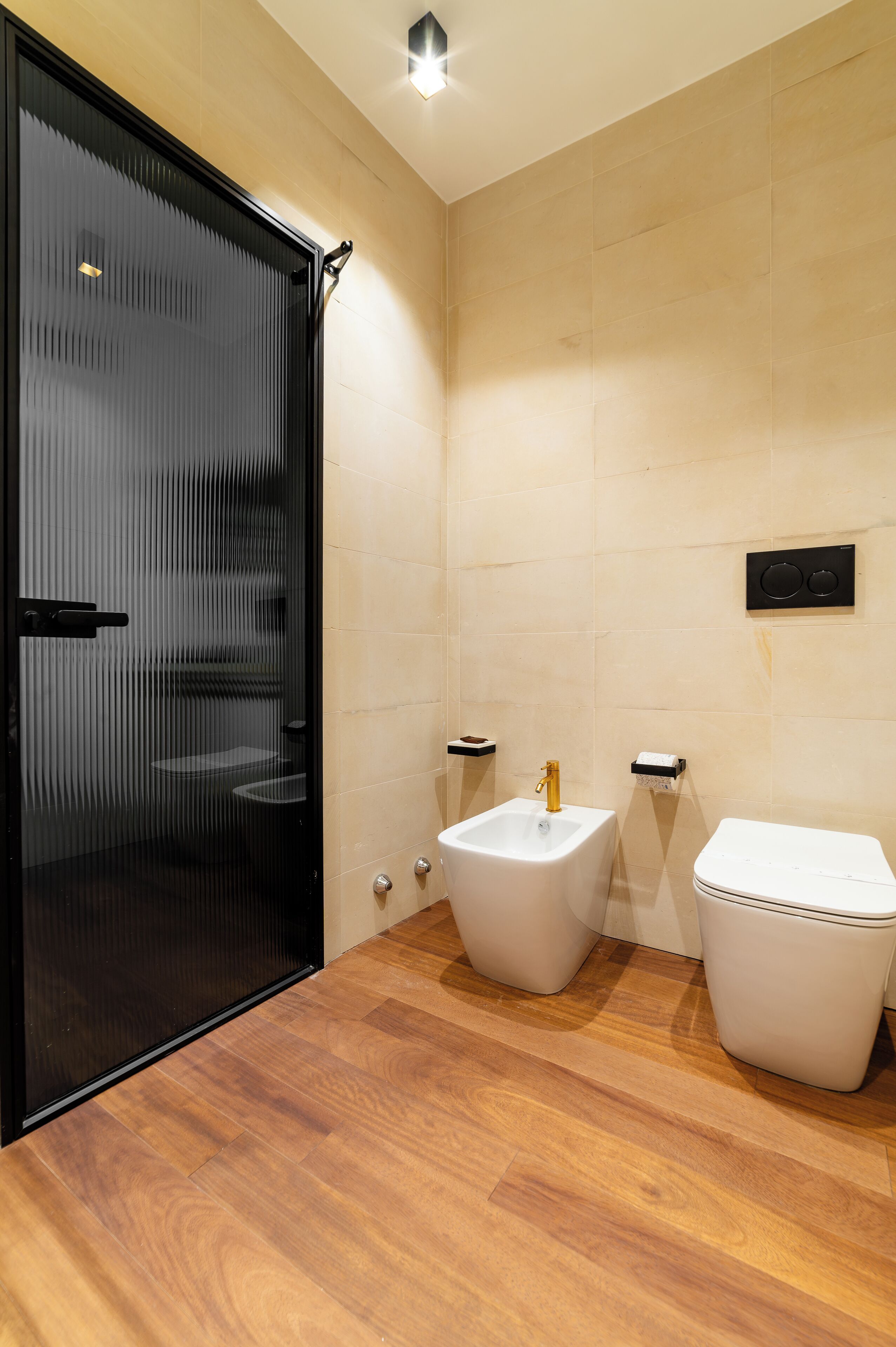Un bagno moderno con pavimento in legno, cabina doccia in vetro, lavandino bianco e un water.