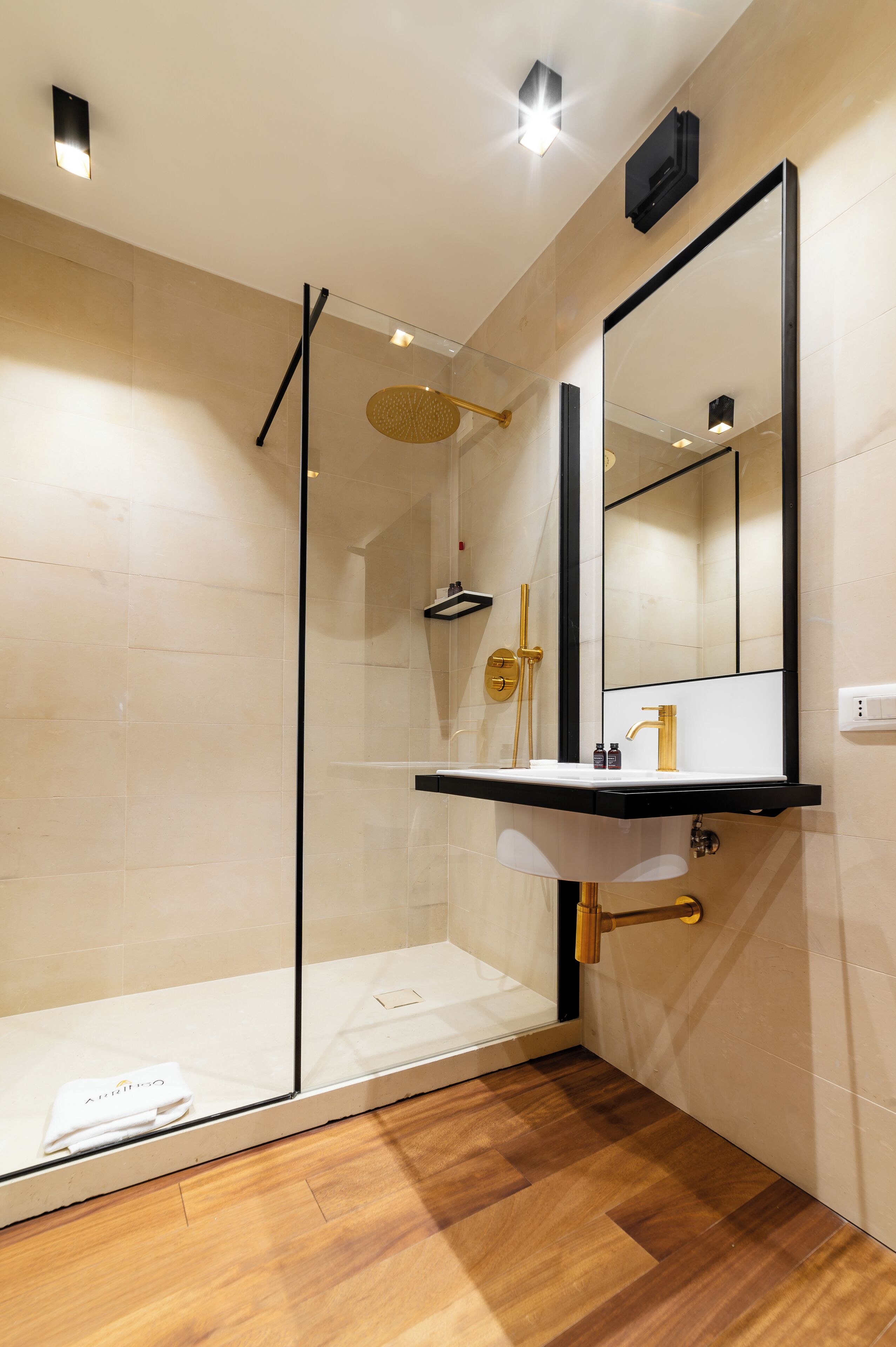 A modern bathroom with a glass-enclosed shower, a sink with a gold faucet, and a large mirror.