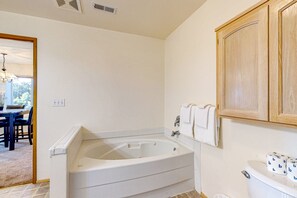 A bathroom with a bathtub, toilet, and wooden cabinet. - Peek-a-boo ocean view home with in-law suite, fireplace, & outdoor space (Coupeville)