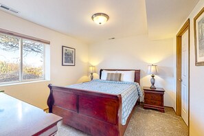 A bedroom with a wooden bed, two bedside tables with lamps, a window with a view of trees, and a door. - Peek-a-boo ocean view home with in-law suite, fireplace, & outdoor space (Coupeville)