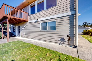 A two-story house with a wooden deck, a small window, and a visible water spigot. - Peek-a-boo ocean view home with in-law suite, fireplace, & outdoor space (Coupeville)