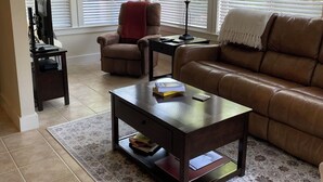 Una sala de estar con un sofá de cuero marrón, una mesa de centro, un sillón rojo y un televisor sobre un mueble bajo.