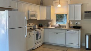 Una cocina con armarios blancos, refrigerador, microondas, horno y lavavajillas.