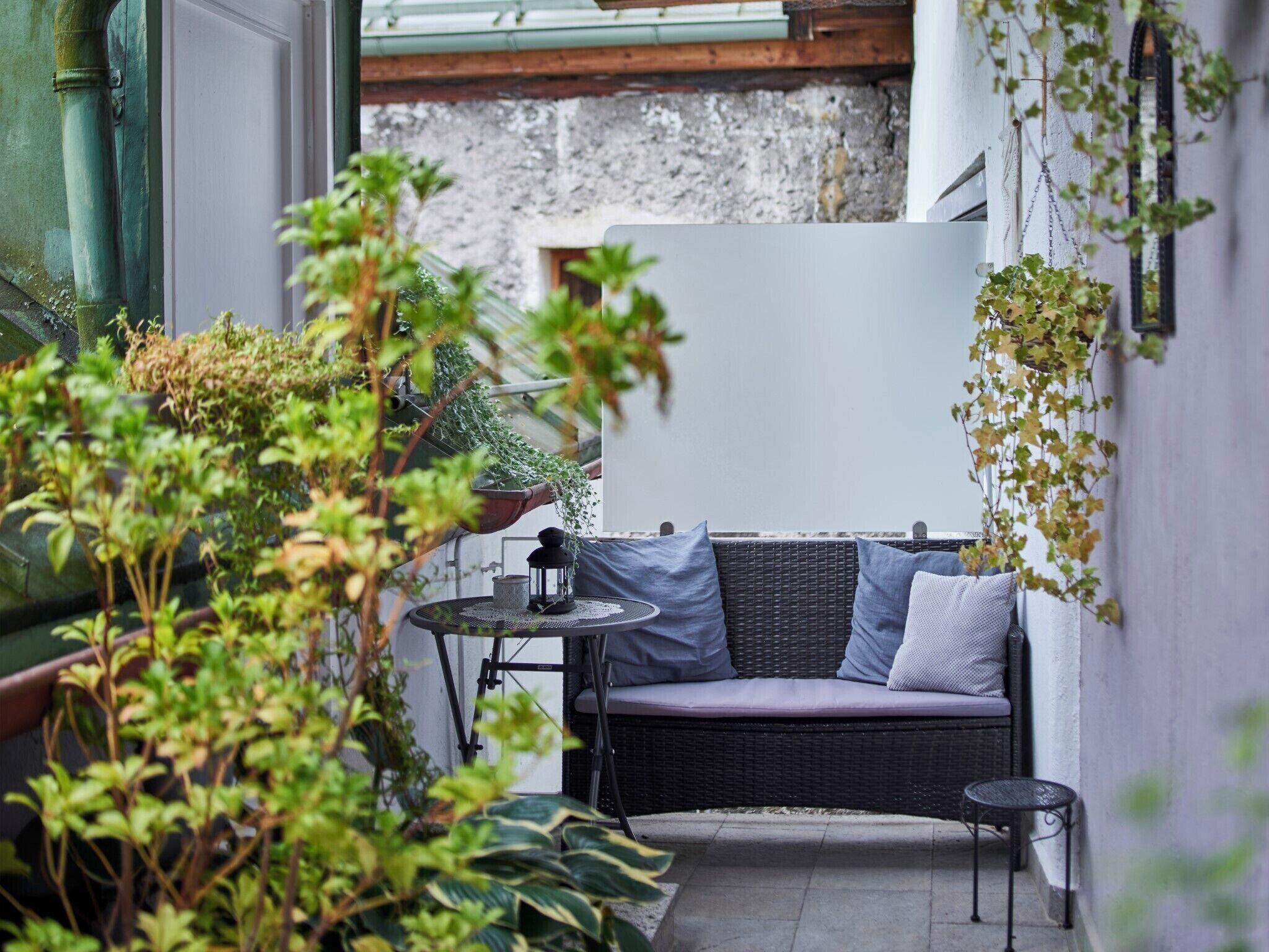 A cozy outdoor seating area with a wicker sofa, a small table, and potted plants.