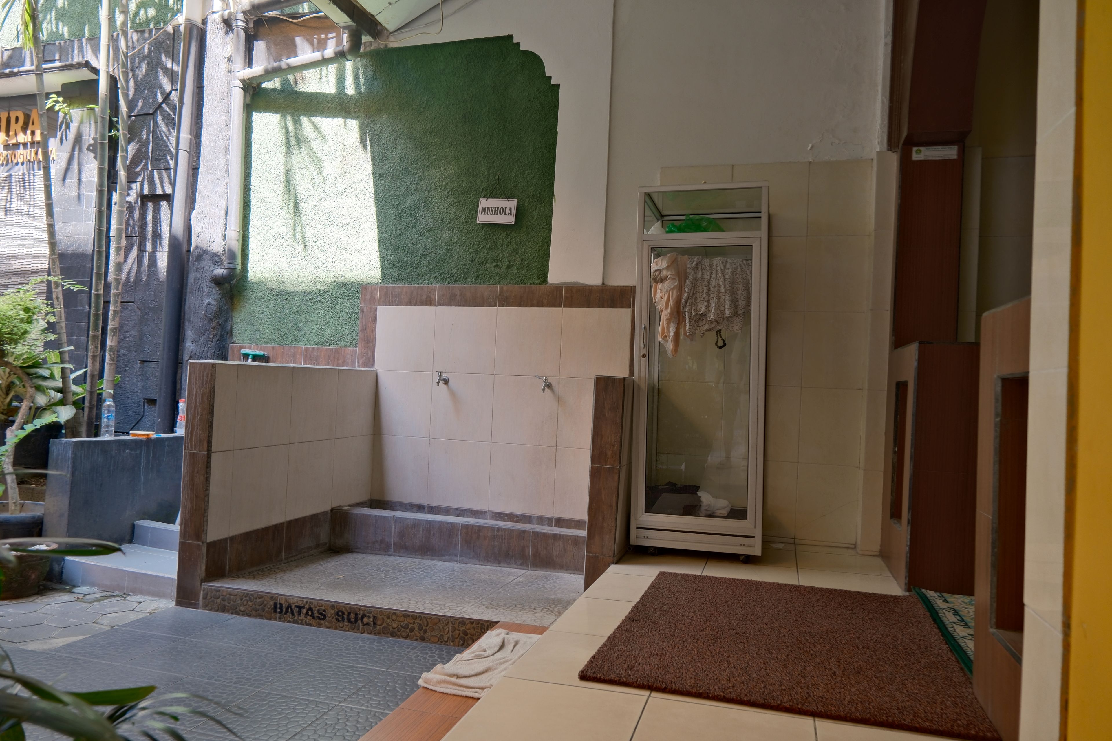 A bathroom with a shower, a towel rack, and a sign reading 'MUSHOLA'.