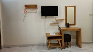 A small, tidy room with a wooden desk, a television mounted on the wall, a mirror, and a small shelf.