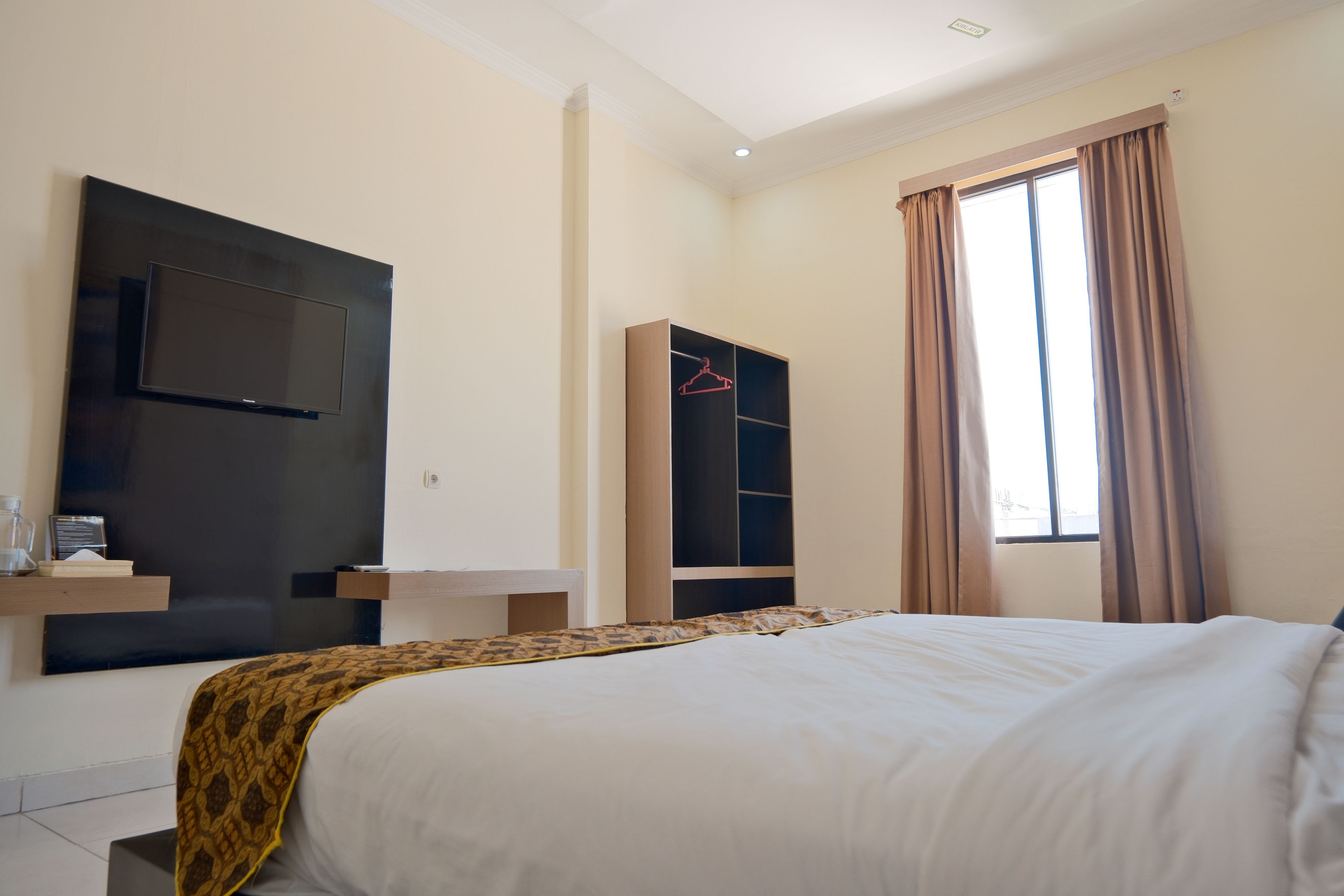 A hotel room with a bed, a TV mounted on the wall, a wardrobe, and a window with curtains.