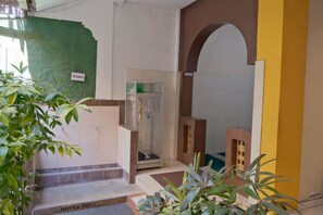 A hotel entrance with a green wall, a sign reading 'MUSHOLA,' and a glass door leading to a room. - Shafira Hotel Yogyakarta (Yogyakarta)