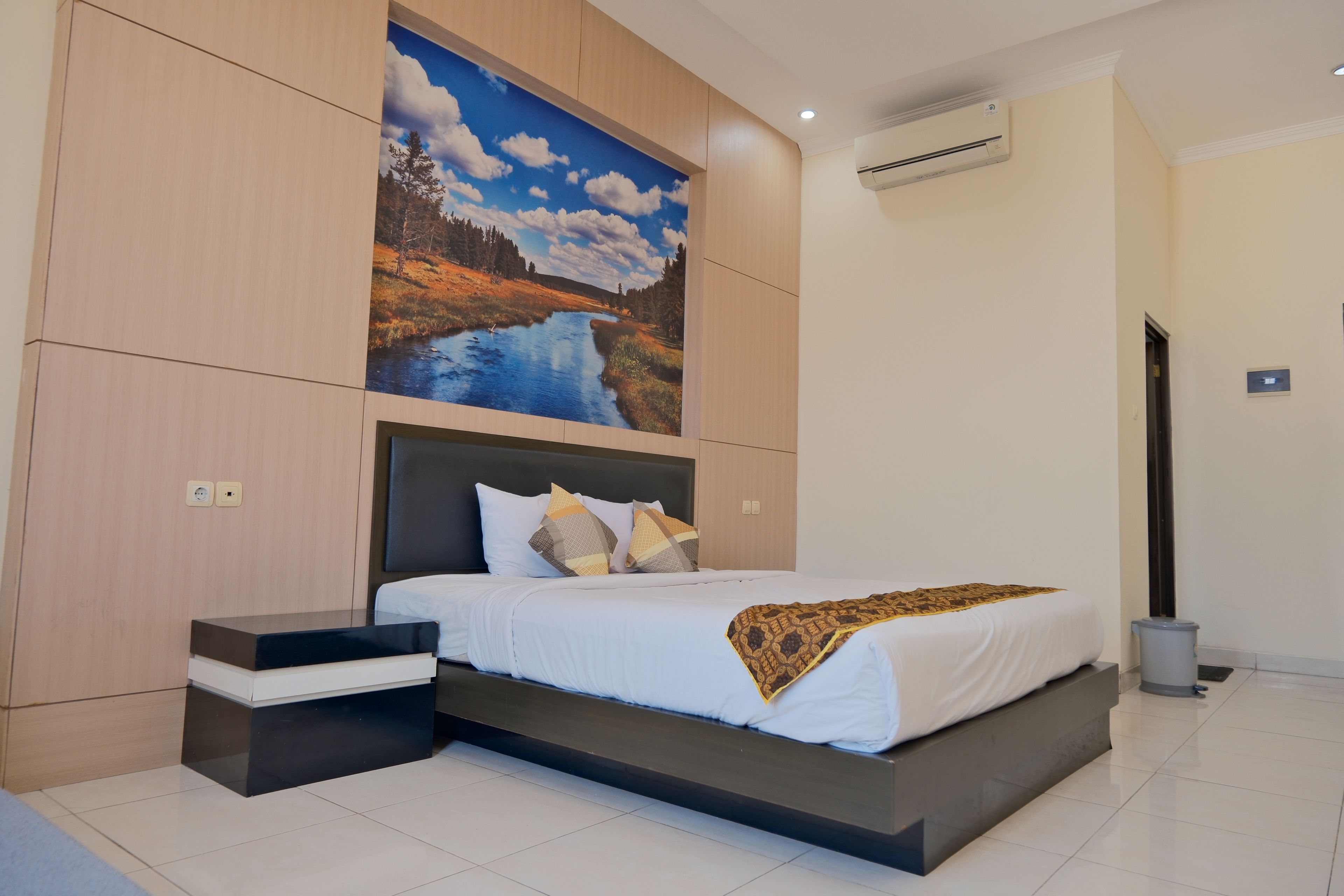 Ein modernes Schlafzimmer mit Bett, Nachttisch, großem Wandbild und Klimaanlage.