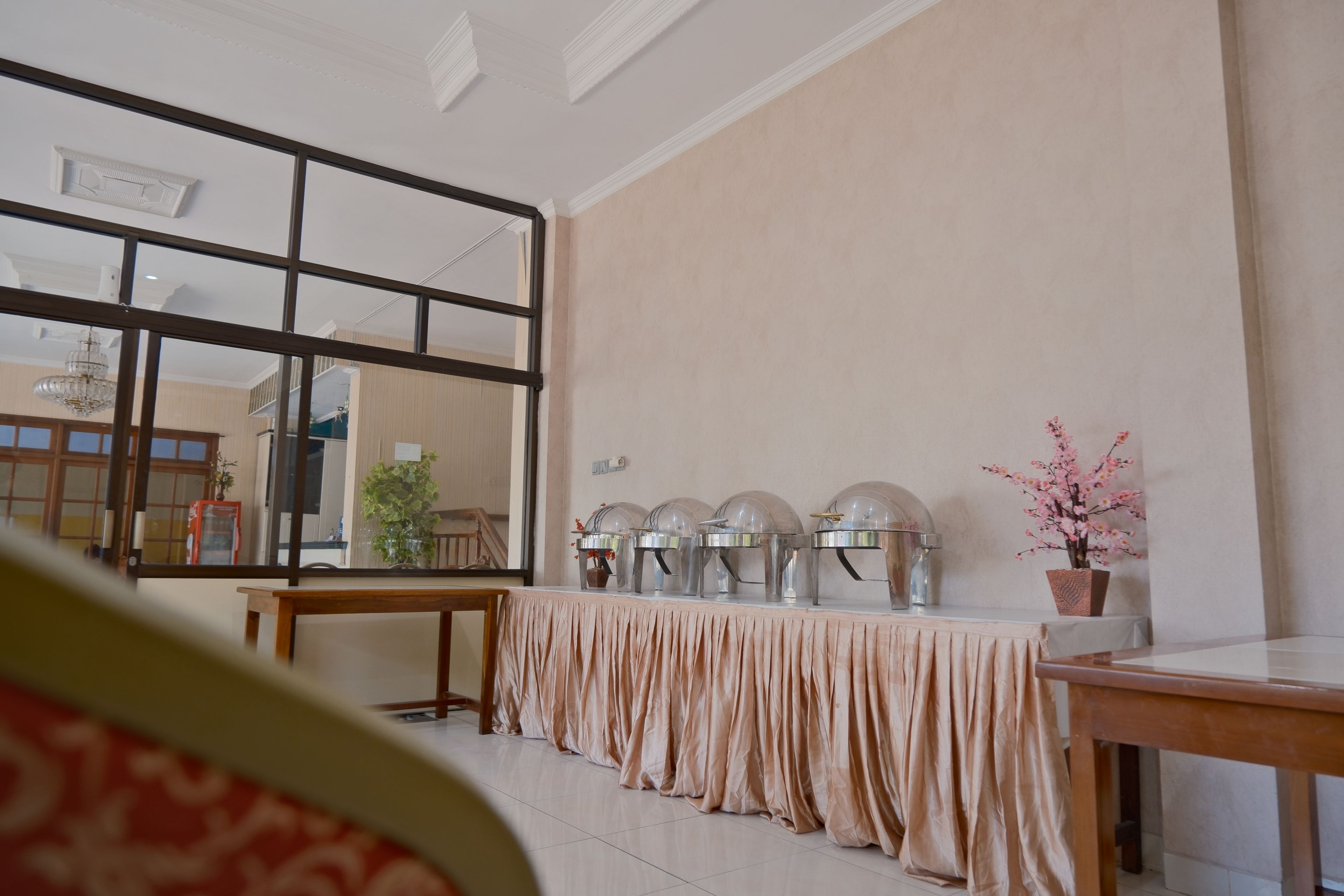 Una habitación con un espejo grande, una mesa con mantel beige y una hilera de equipos para servicio de alimentos.