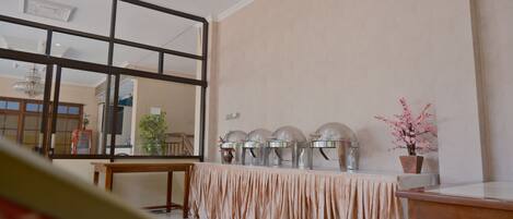 Una habitación con un espejo grande, una mesa con mantel beige y una hilera de equipos para servicio de alimentos.