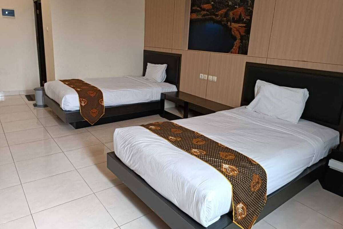 Una habitación de hotel con dos camas, un cuadro grande en la pared y suelo de baldosas.