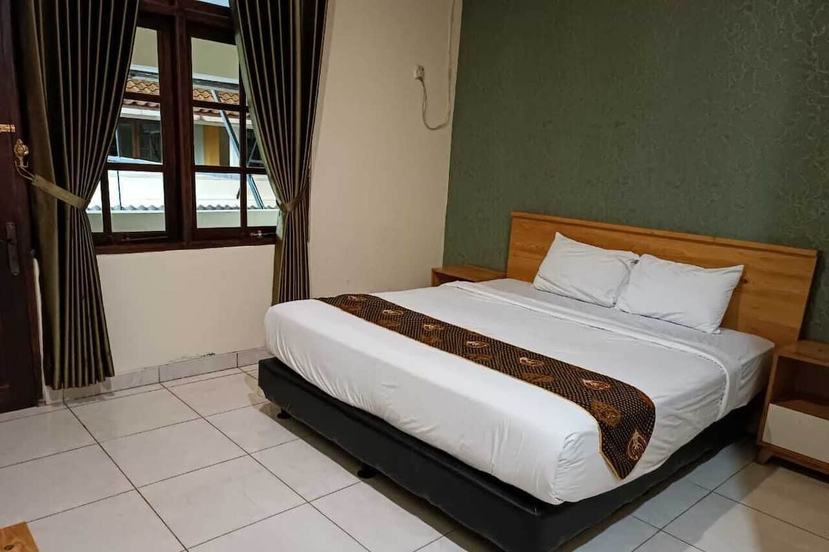 Una habitación de hotel con cama, cortinas, cabecero de madera y pared verde.