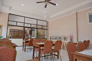 A dining area with multiple tables and chairs, a ceiling fan, and a large window with a view of the outside. - Shafira Hotel Yogyakarta (Yogyakarta)