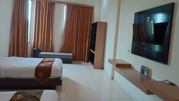 A hotel room with two beds, a TV mounted on the wall, a desk, and a large window with curtains.