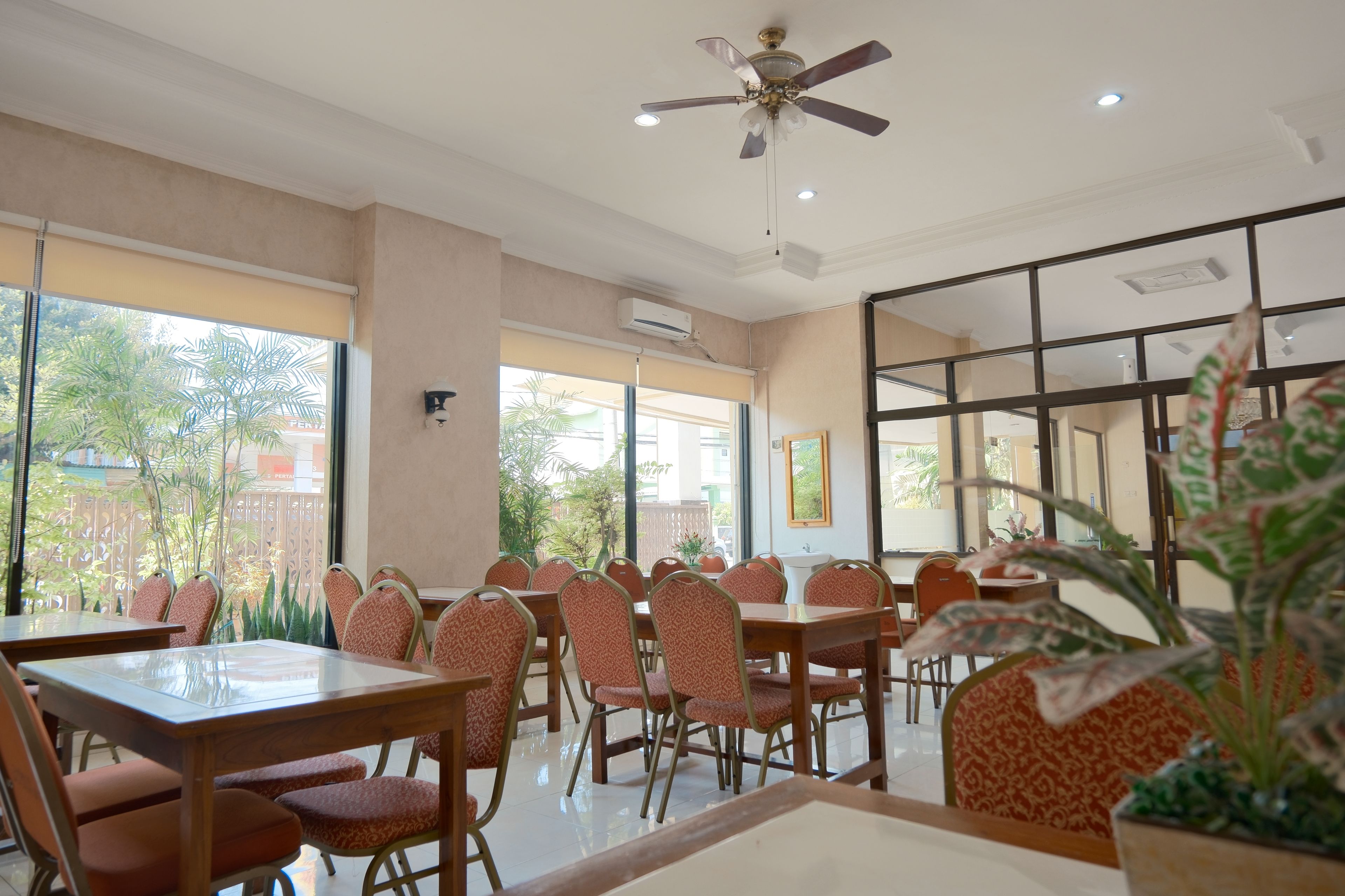 A restaurant with multiple tables and chairs, large windows, and a ceiling fan.