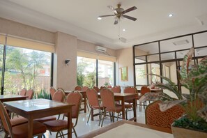 Un restaurante con varias mesas y sillas, amplias ventanas y un ventilador de techo.