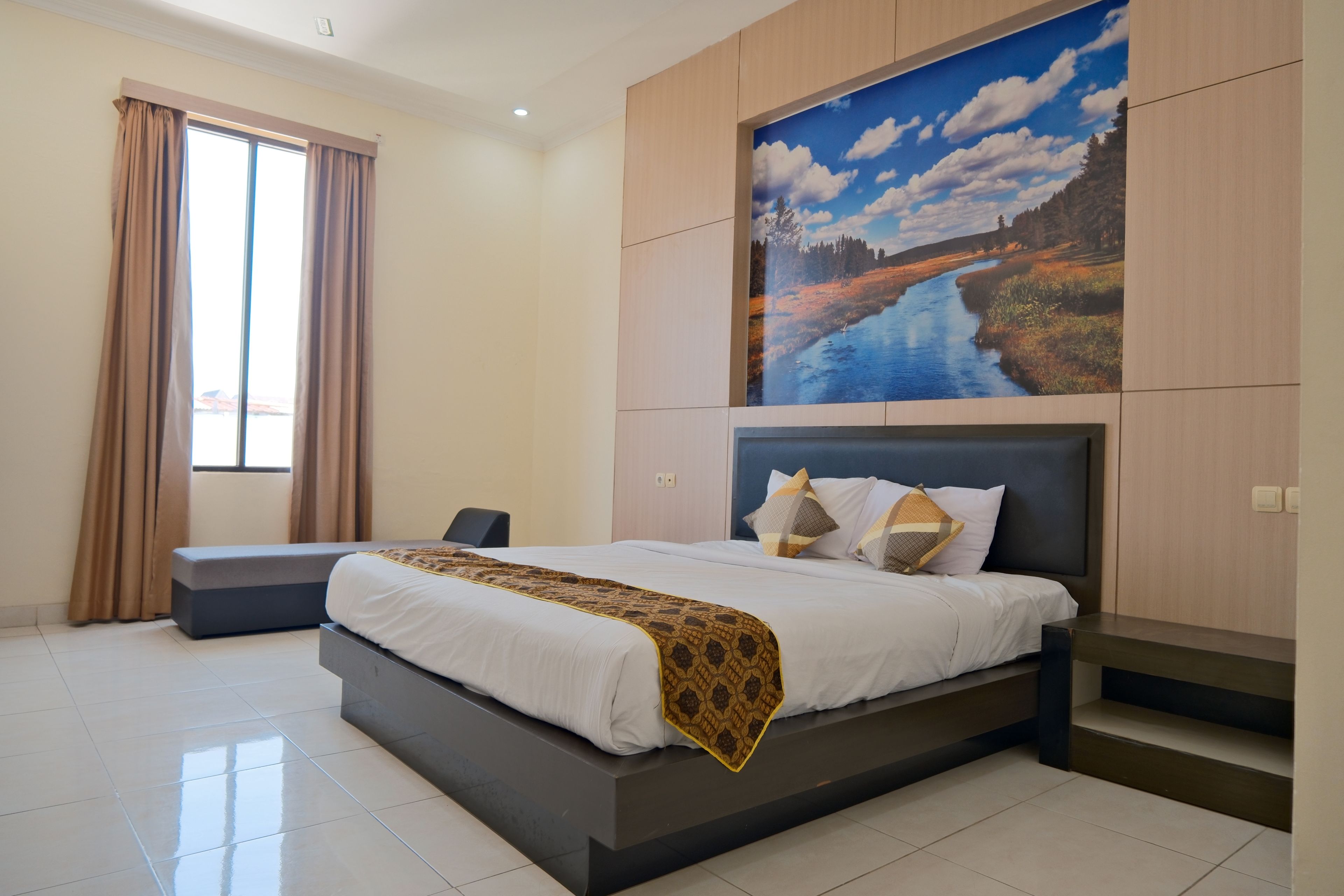 A modern bedroom with a large bed, a headboard with a painting, a bench, and a window with curtains.