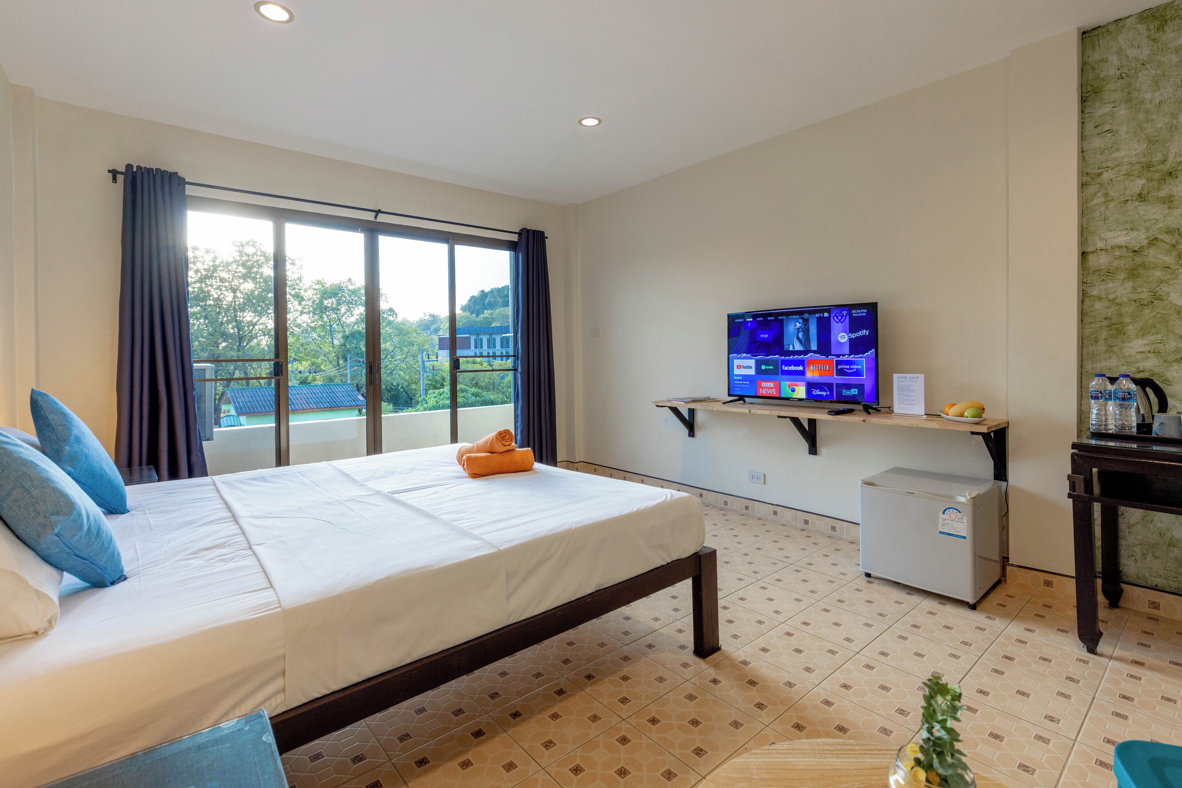 Habitación de hotel con cama, televisor sobre un mueble, refrigerador pequeño y ventana con cortinas.