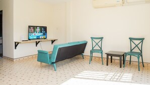A small room with a teal sofa, two teal chairs, a small table, and a TV on a shelf. - Club 22 Kamala Suites (Kamala)