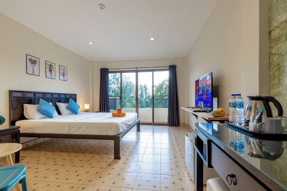 A hotel room with a bed, a TV, a desk with a coffee maker, and a view of the outdoors.