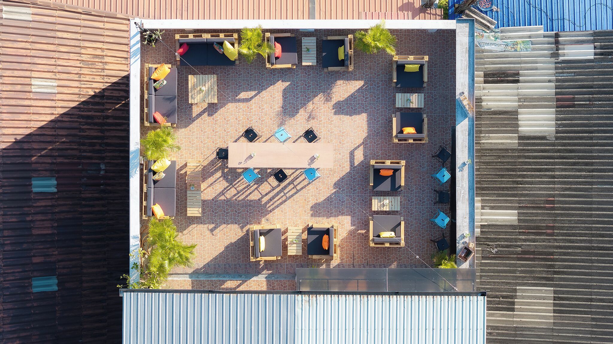 An aerial view of a rooftop patio with seating areas, a table, and potted plants.