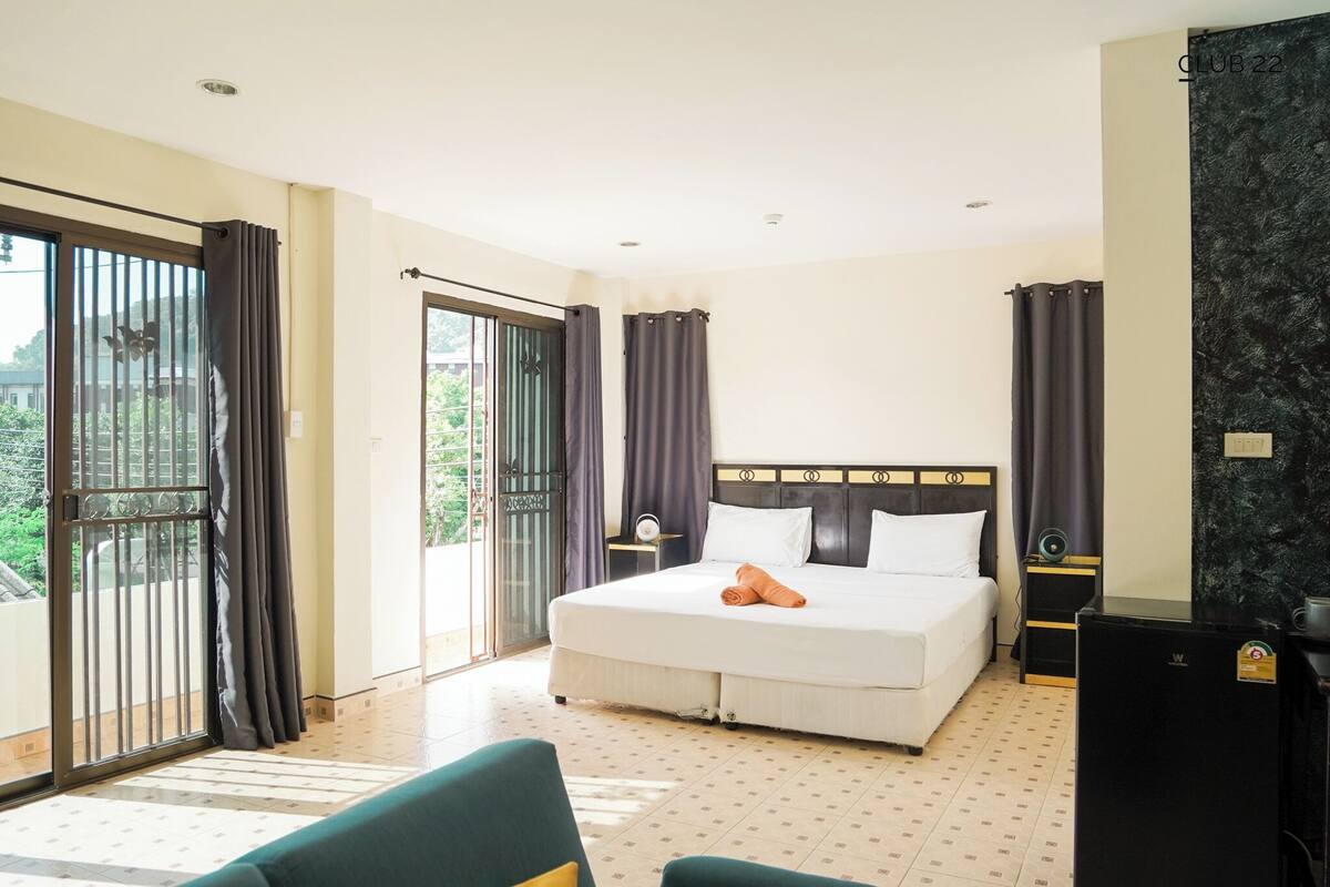 A hotel room with a large bed, a desk, a chair, and a balcony with curtains.