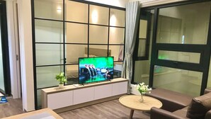 A modern living room with a large flat-screen TV, a sofa, a small round coffee table, and a large window with curtains. - Funhome Bo Song Set Apartment Ha Noi (Hanoi)