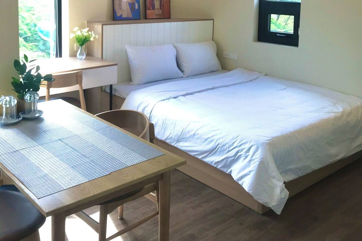 A bedroom with a bed, a desk, and two paintings on the wall.