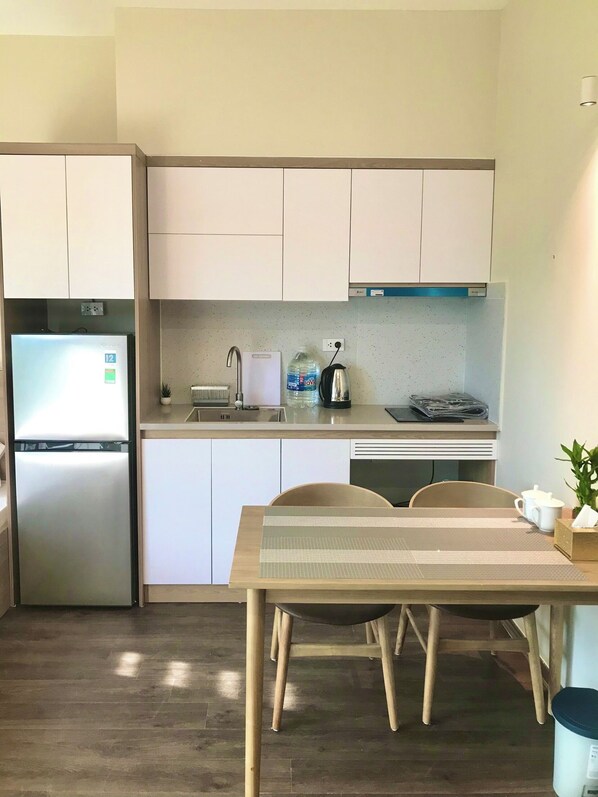 A modern kitchen with white cabinets, a stainless steel refrigerator, a sink, and a dining area with a table and chairs.