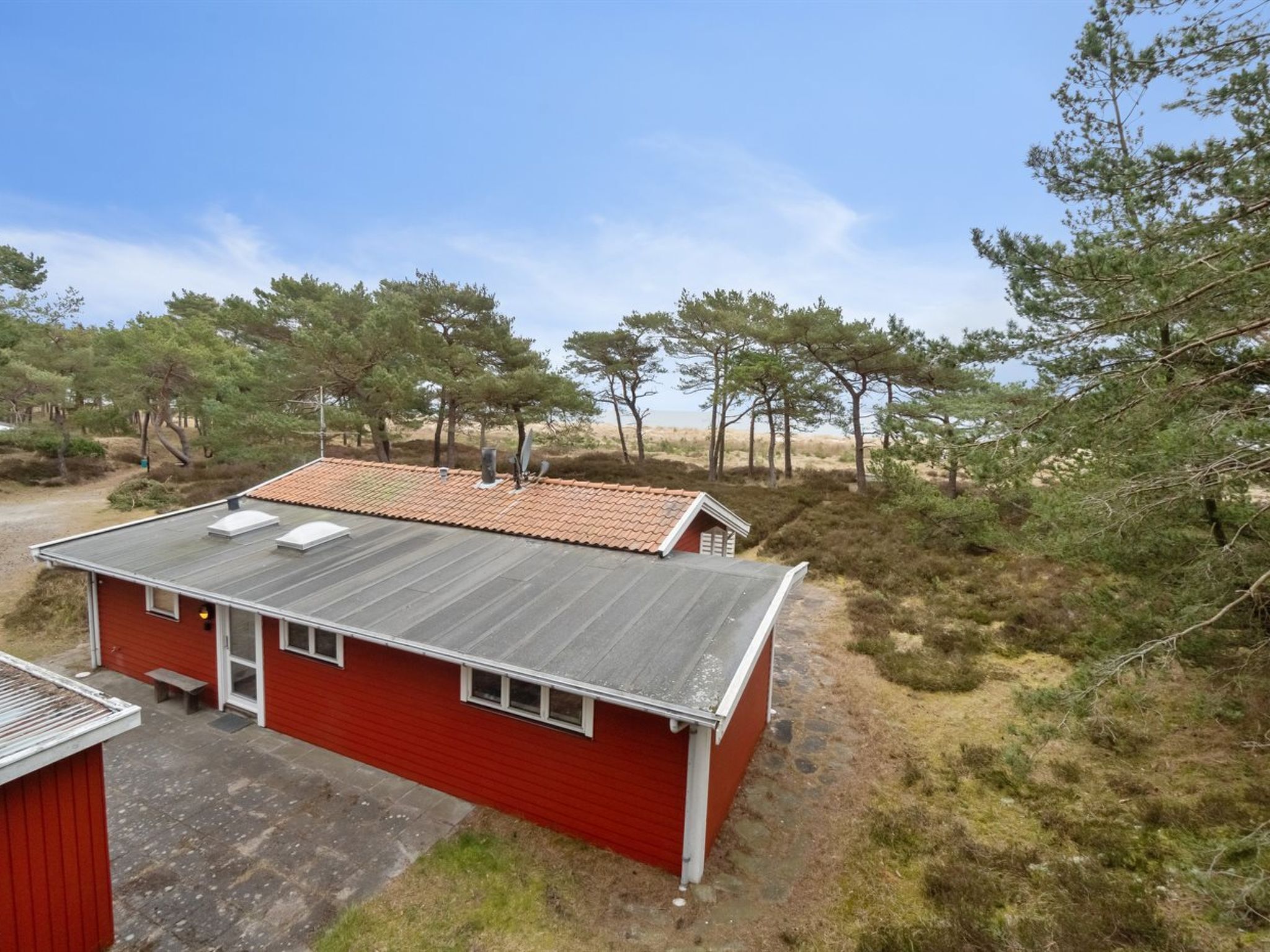 Un bâtiment rouge avec un toit en métal, entouré d’arbres et bordé d’un paysage sablonneux.