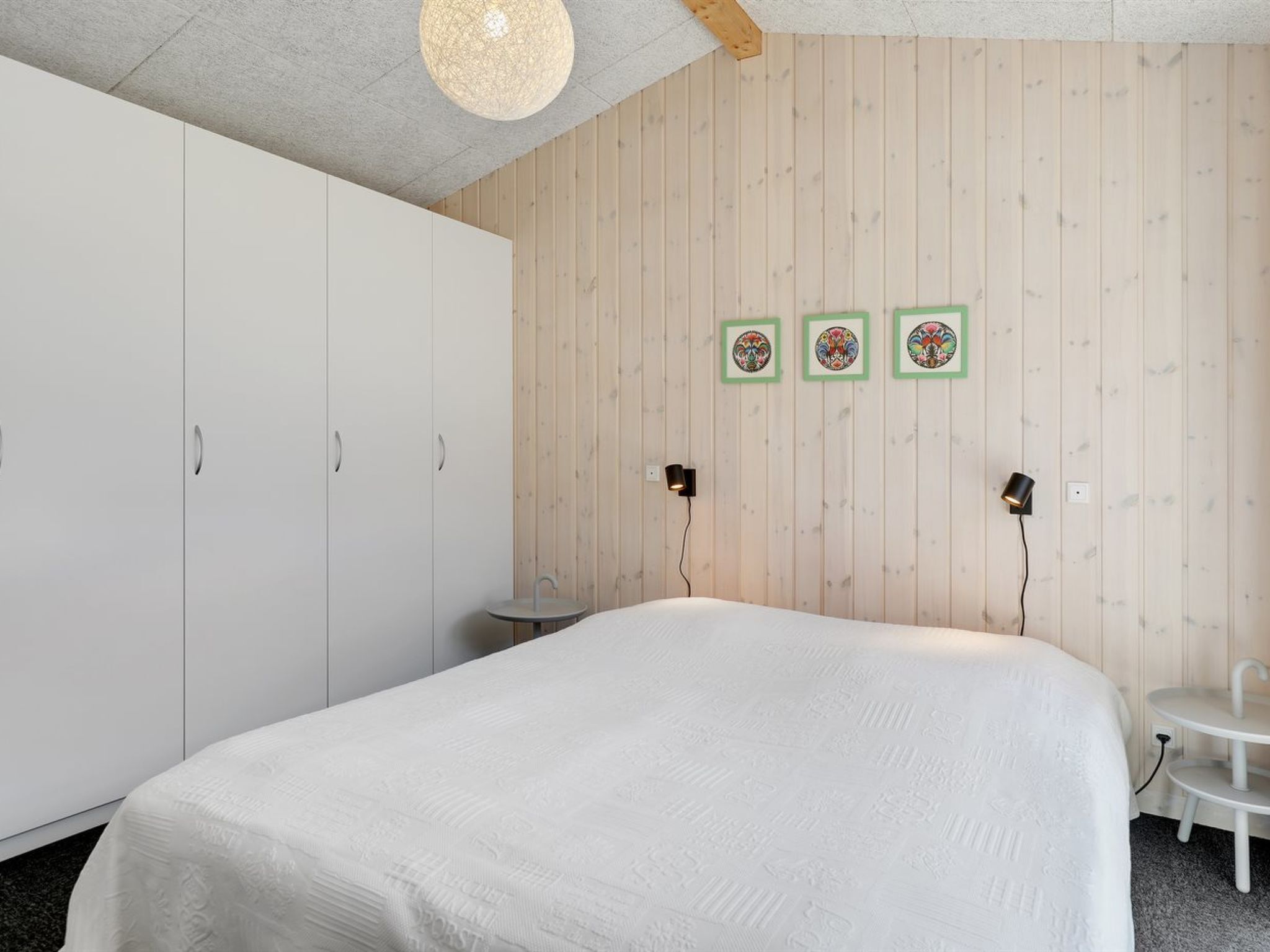 A bedroom with a large bed, wooden panel walls, and three framed artworks.