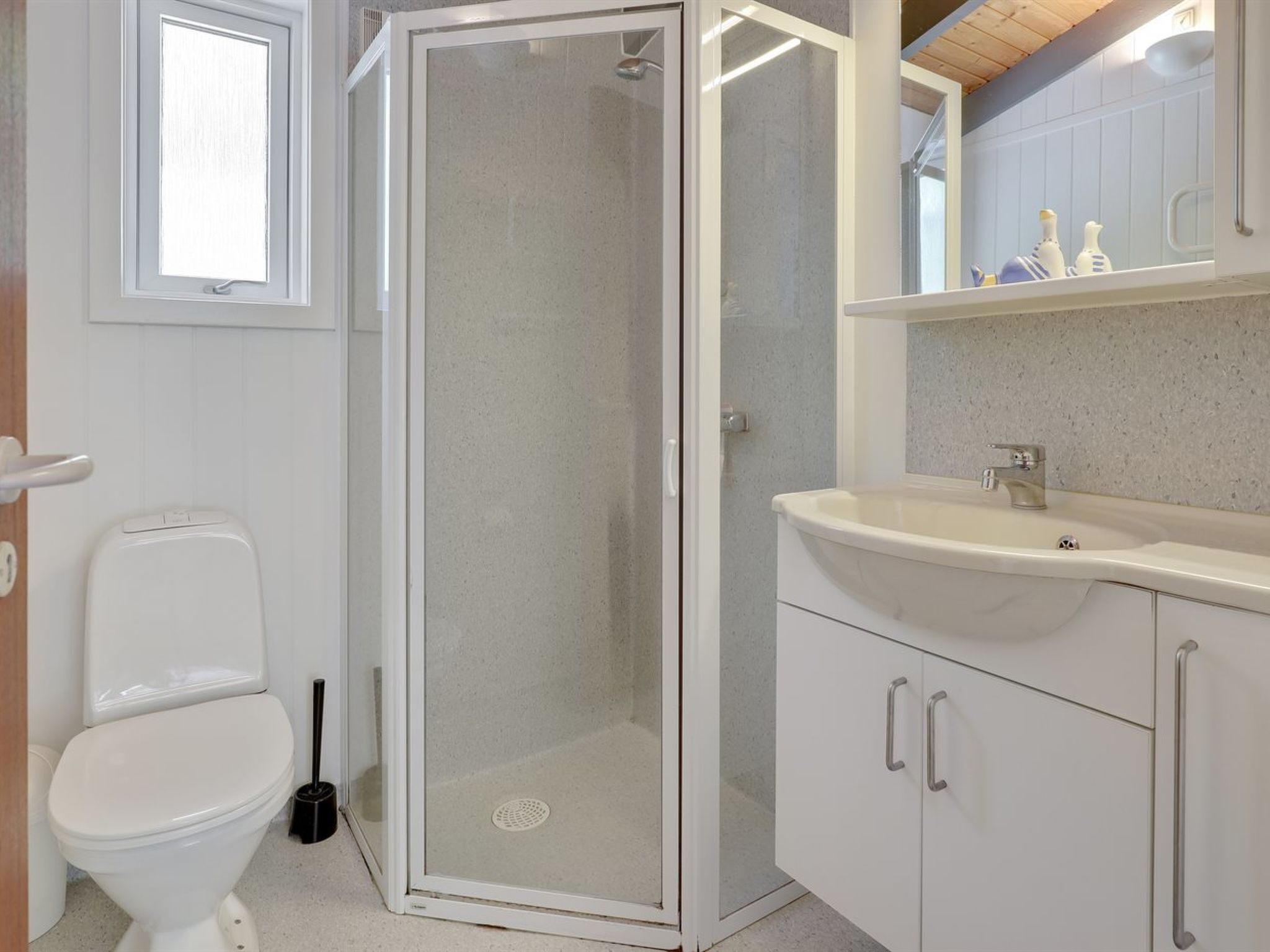 Een badkamer met een douche in een glazen cabine, toilet, wastafel met spiegel erboven en een plank met toiletartikelen.