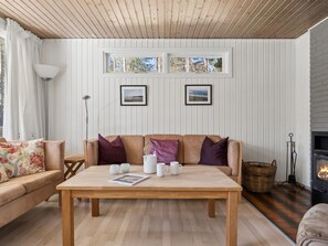 Una sala de estar acogedora con una mesa de madera, dos sofás, una chimenea y cuadros en la pared.