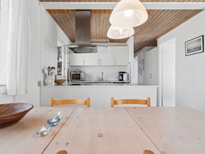 A modern kitchen with white cabinets, a wooden ceiling, and a dining area with a wooden table and chairs.