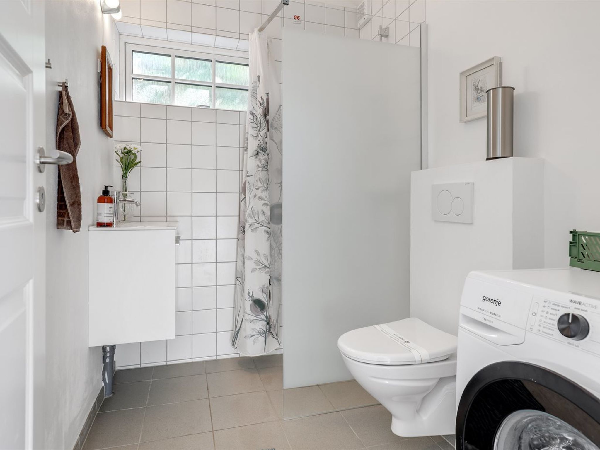 A modern bathroom with a toilet, washing machine, and a shower area.