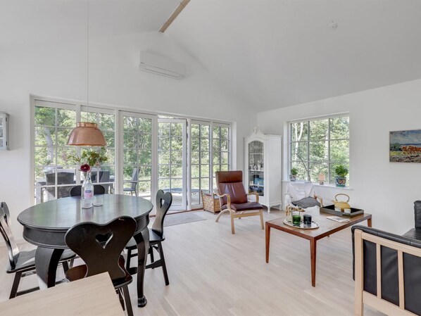 A spacious living room with a round dining table, a fireplace, and large windows offering a view of the outdoors.