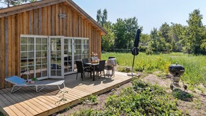 En stuga av trä med en veranda, utomhusmöbler och en grill.