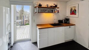 Ett modernt kök med vita skåp, en träbänkskiva och en inbyggd hylla ovanför diskbänken.