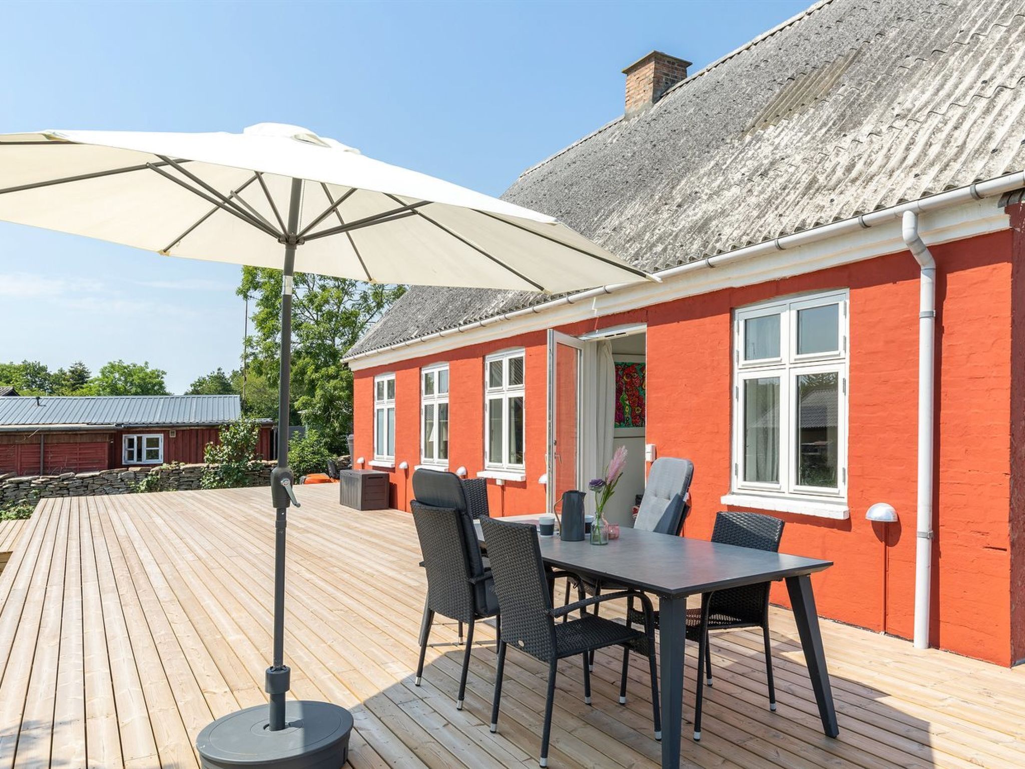 Ein rotes Gebäude mit einer Holzterrasse, Außenbestuhlung und einem großen Sonnenschirm.