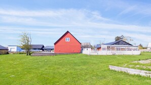 En röd ladugård på en gräsklädd åker, med ett vitt staket och en blå byggnad i bakgrunden.