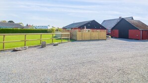 A gravel parking area with a wooden fence, a red barn, and a black barn in a rural setting. - "Kiana" - 250m from the sea by Interhome (Nexø)