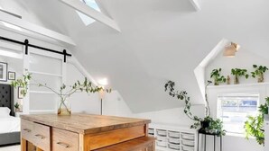 A modern bedroom with a loft-style ceiling, a wooden desk, and multiple potted plants. - Capitola Village Work-Live Loft - Pet Friendly (Capitola)