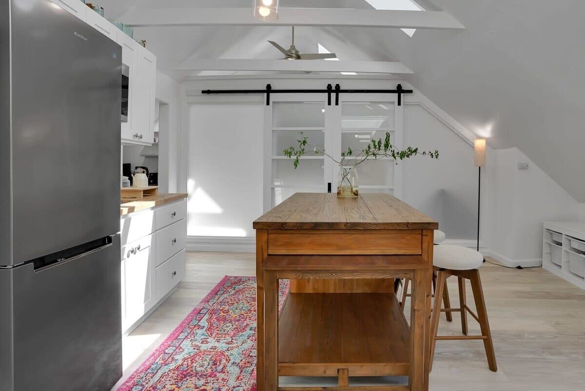 Una cocina moderna con una mesa de madera, armarios blancos y un tapete colorido.