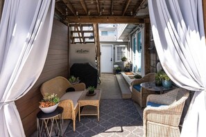 Ein überdachter Patio-Bereich mit Korbmöbeln, einem Grill und einem Willkommensschild.