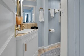 Een badkamer met een wit wastafel, een gouden kraan en een spiegel. Handdoeken hangen aan een rek en er is een toiletpapierhouder aan de muur.