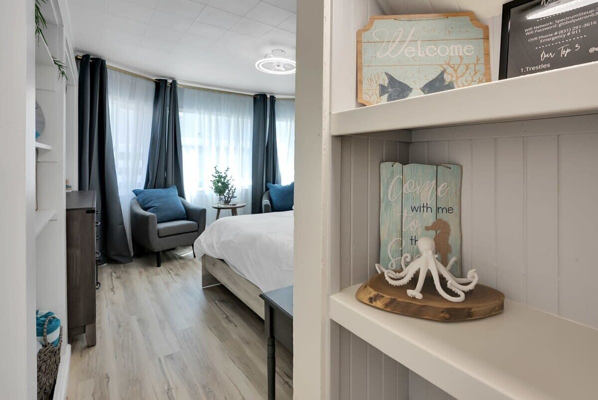A hotel room with a bed, a chair, a small table, and a decorative welcome sign.