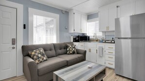 A modern kitchen with white cabinets, a stainless steel refrigerator, and a grey sofa with patterned cushions. - Capitola Village Hideaway Bungalow - Pet friendly! (Capitola)