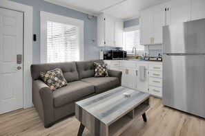 Een moderne keuken met witte kasten, een roestvrijstalen koelkast en een grijze bank met gestreepte kussens.