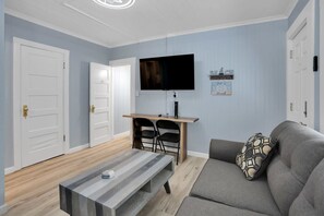 A living room with a gray sofa, a coffee table, a TV on a wooden stand, and two black chairs. - Capitola Village Hideaway Bungalow - Pet friendly! (Capitola)